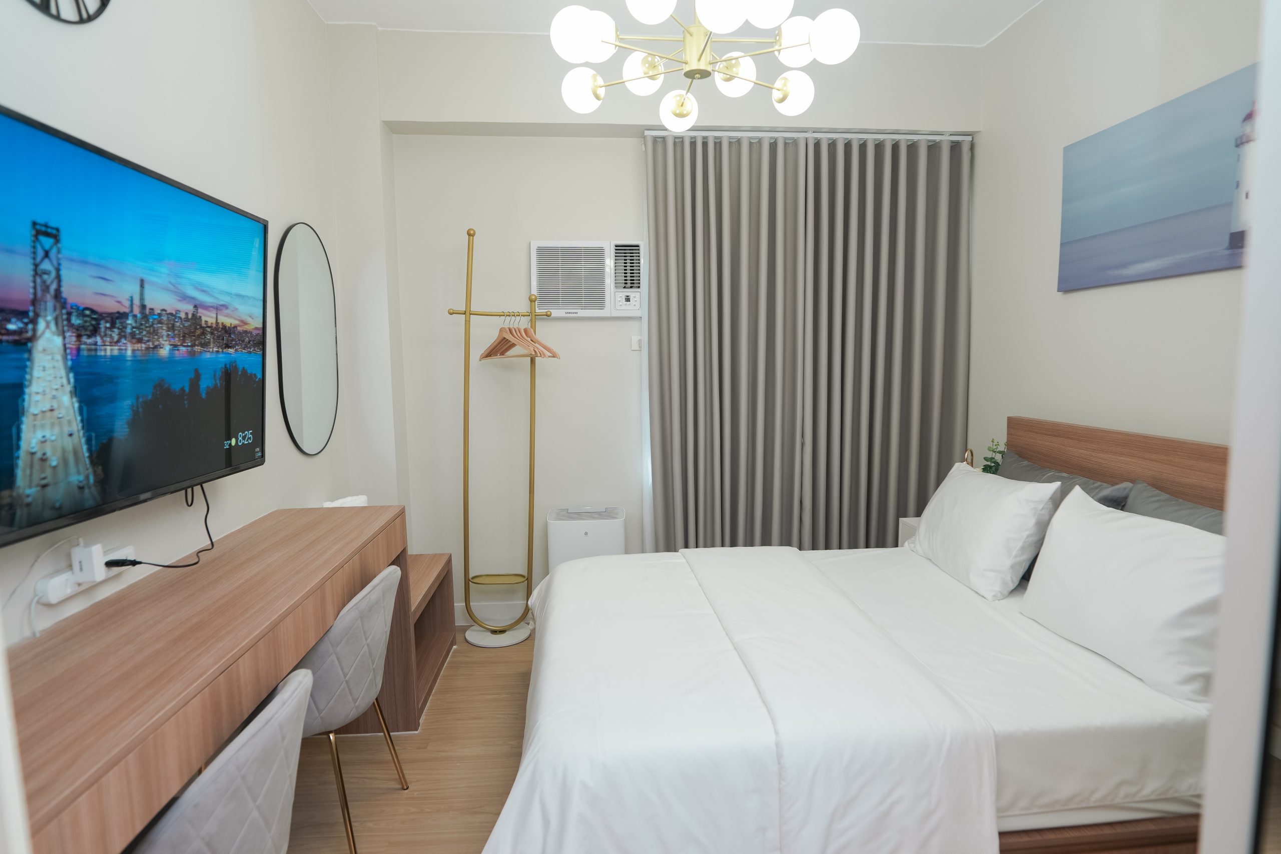 The bedroom with queen size bed and a painting mounted on the wall above the headboard. The 55-inch smart TV on the left side and beside it an oval mirror.