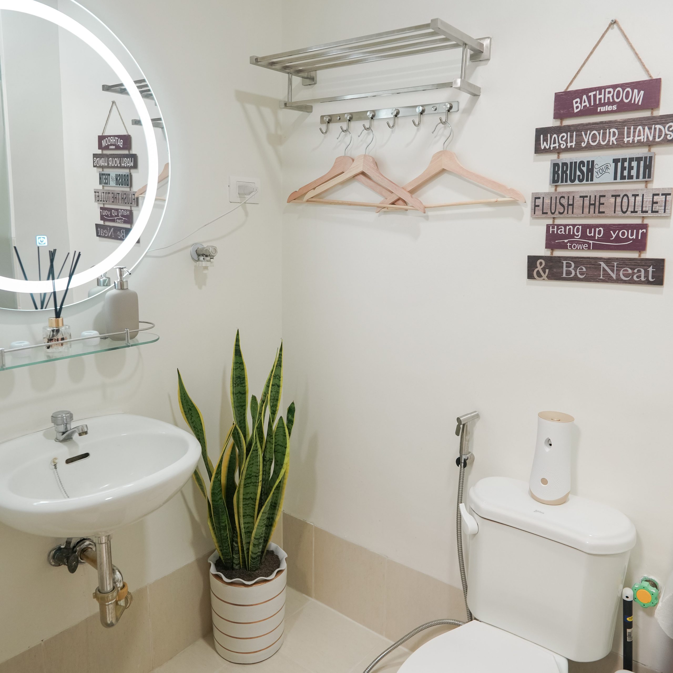 A clean restroom with a plant under the sink and a round mirror that has led lights around it. And a plant under the sink.